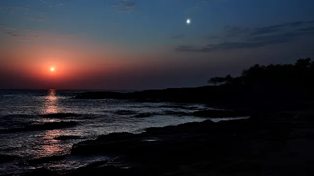 Water, Sky, Cloud, Atmosphere, Light, Natural environment, Moon, Afterglow, Dusk, Sunlight, Tree, Coastal and oceanic landforms, Sunset, Sunrise, Beach, Astronomical object, Atmospheric phenomenon, Plant, Horizon, Landscape